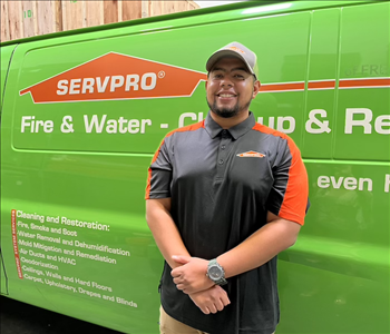 male employee wearing a hat standing in front of a SERVPRO van