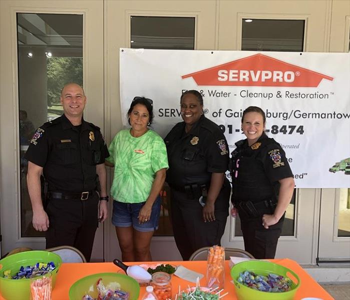 Policeman and policewomen and SERVPRO employee standing behind table with candy